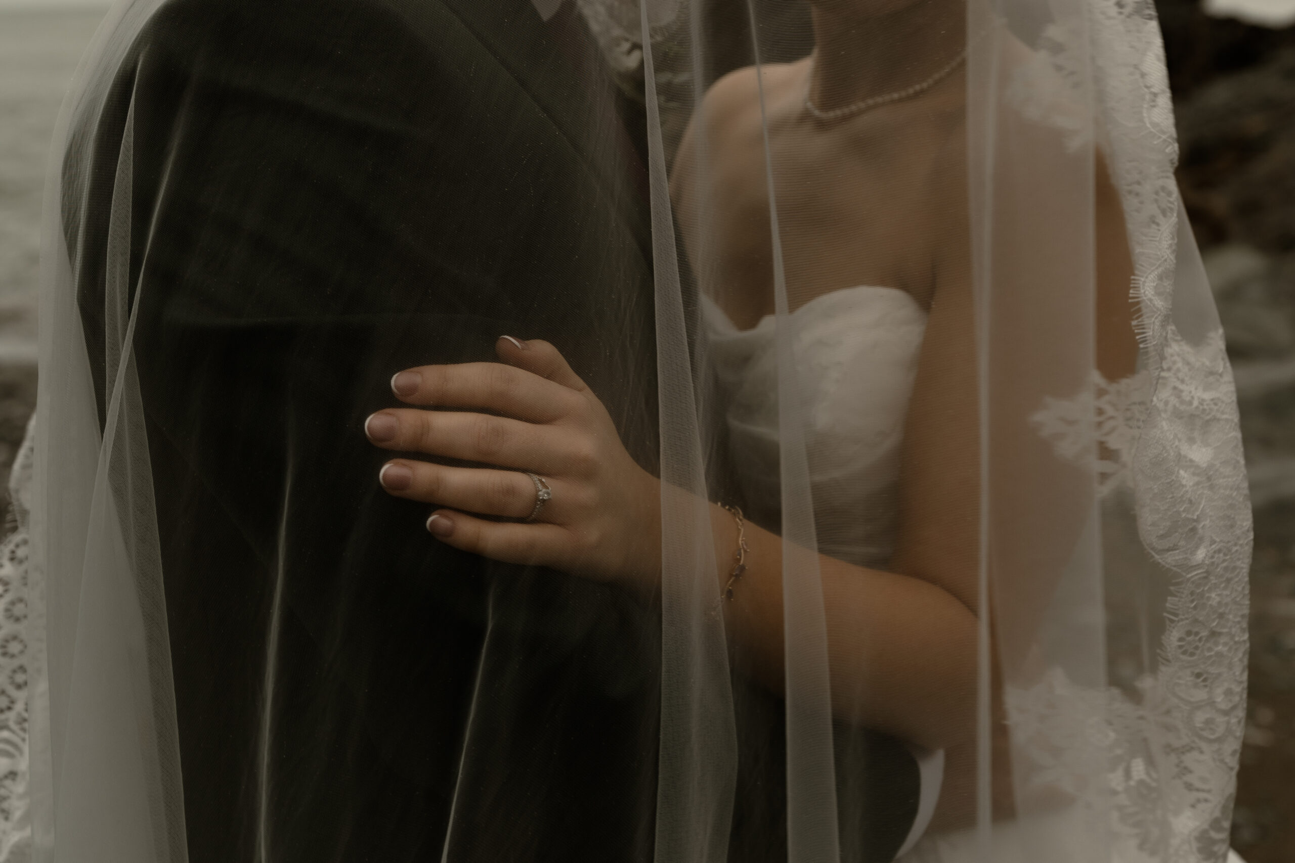 Cinematic photo of bride and grooms hands under a wedding veil, taken at Polhawn Fort in Cornwall